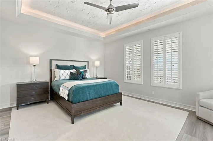 Tray ceiling with recessed lighting, central brushed nickel ceiling fan, and windows outfitted with interior plantation shutters
