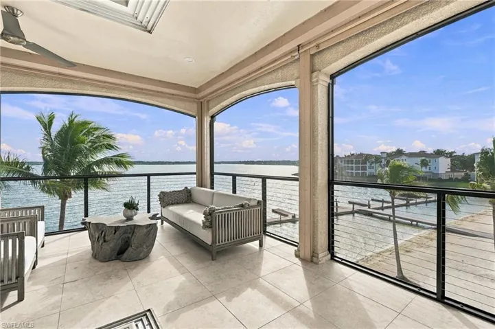 Covered balcony featuring tile flooring, a built-in ceiling fan, arched structural openings, and a metal cable railing system overlooking the water