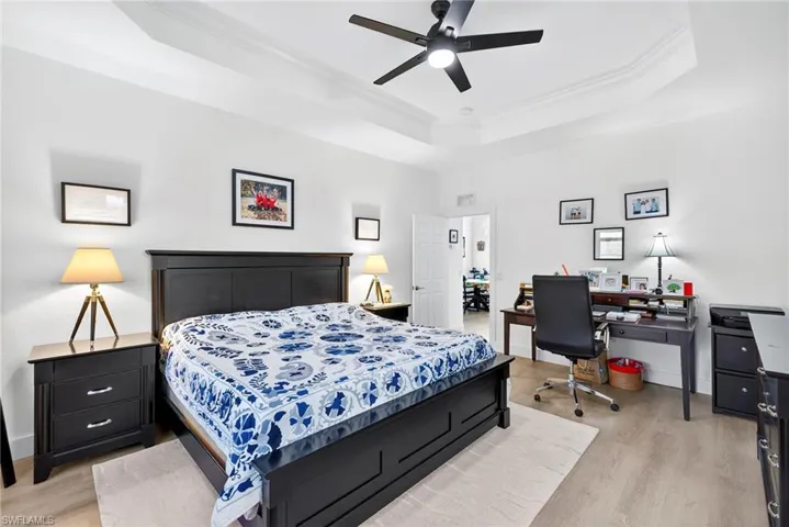 Guest Bedroom featuring crown molding, light wood finished floors, a tray ceiling, an office area, and a ceiling fan