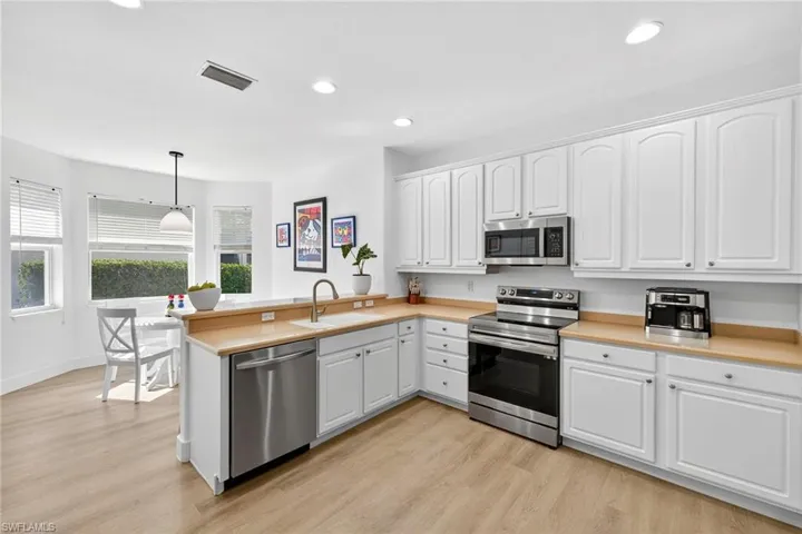 Kitchen with appliances with stainless steel finishes, a peninsula, white cabinets, light countertops, and decorative light fixtures