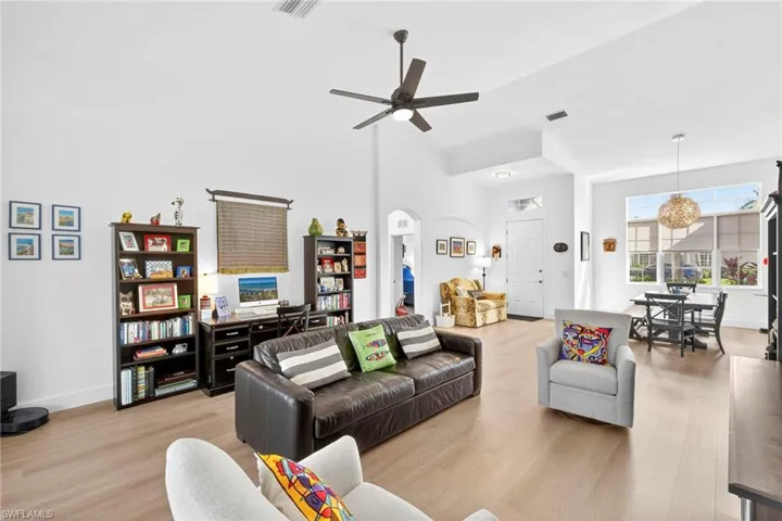 Living room with light wood-type flooring, ceiling fan, arched walkways, and vaulted ceiling