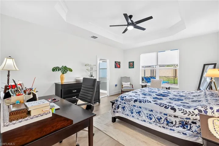 Bedroom featuring light wood finished floors, a tray ceiling, a ceiling fan, crown molding, and an office area