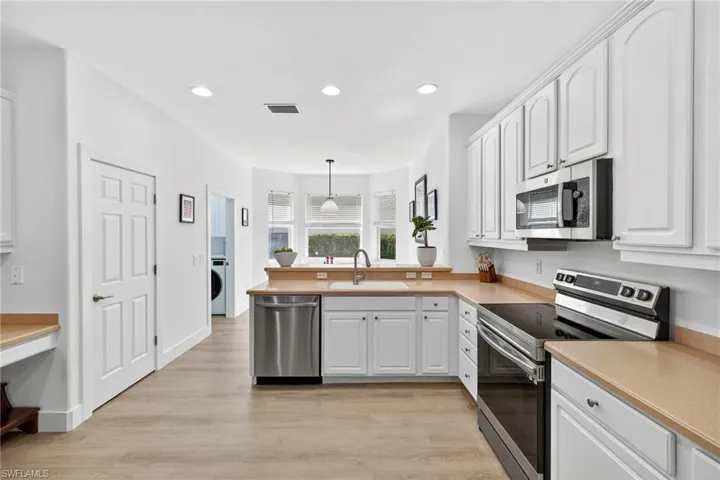 Kitchen with appliances with stainless steel finishes, light countertops, decorative light fixtures, light wood-style flooring, and white cabinets