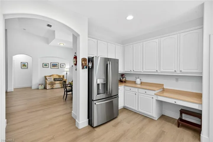 Kitchen featuring stainless steel refrigerator with ice dispenser, light countertops, light wood finished floors, white cabinetry, and built in study area