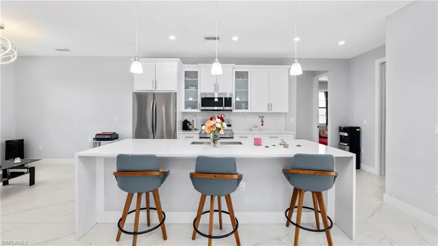 Kitchen featuring white cabinets, glass insert cabinets, stainless steel appliances, a large island with sink, and light stone counters