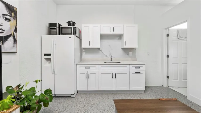 Kitchen with white cabinetry, white refrigerator with ice dispenser, dark speckled floor, and light stone counters