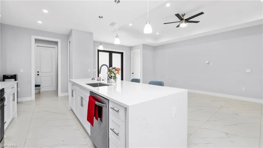 Kitchen with light stone countertops, ceiling fan, a kitchen island with sink, stainless steel dishwasher, and hanging light fixtures