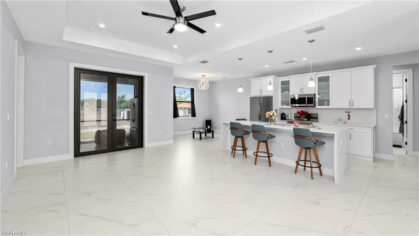 Kitchen with white cabinetry, glass fronted cabinets, light marble finish flooring, ceiling fan, and a breakfast bar area