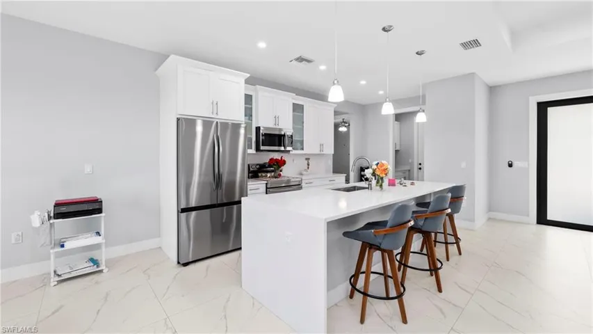 Kitchen featuring stainless steel appliances, glass insert cabinets, a kitchen breakfast bar, light marble finish floors, and white cabinets