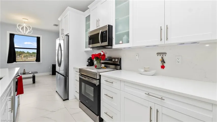 Kitchen featuring stainless steel appliances, glass insert cabinets, white cabinets, light marble finish flooring, and light stone countertops