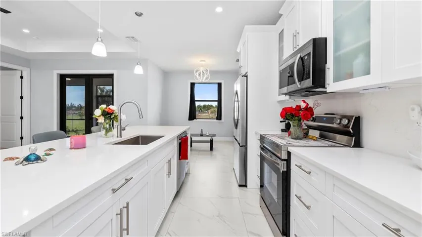 Kitchen with stainless steel appliances, white cabinetry, glass fronted cabinets, decorative light fixtures, and light stone counters