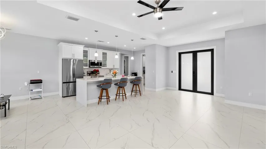 Kitchen with light marble finish flooring, an island with sink, stainless steel appliances, a kitchen breakfast bar, and glass insert cabinets