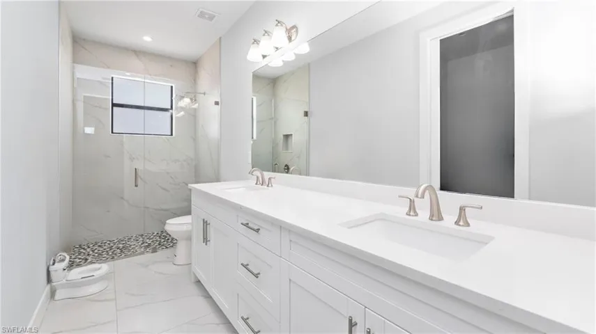 Bathroom featuring double vanity, a marble finish shower, light marble finish flooring, and recessed lighting