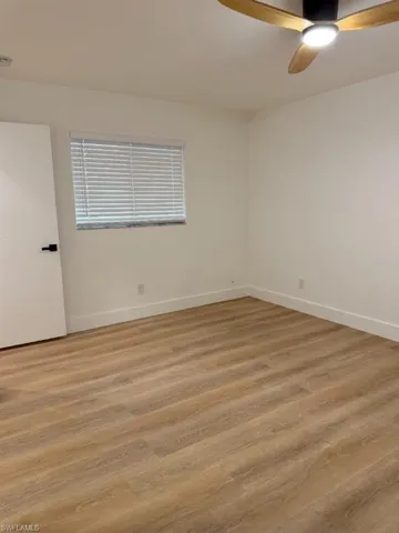 Spacious room featuring wood-finish flooring, crisp white walls, and a contemporary ceiling fan with integrated lighting