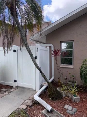 Exterior featuring a palm tree, white vinyl fencing, stucco siding, and a single window