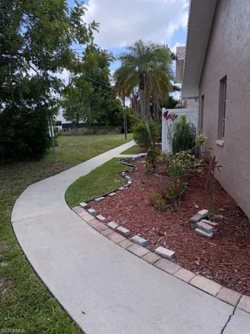 Curved concrete pathway bordering a mulched garden bed with various plantings