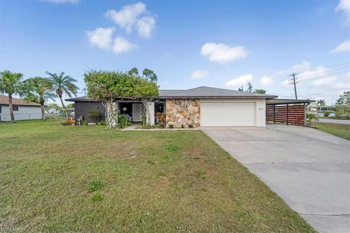View of front of house with a front yard, fence, stone siding, an attached garage, and driveway