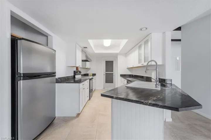 Kitchen with a sink, dark countertops, appliances with stainless steel finishes, a peninsula, and a tray ceiling