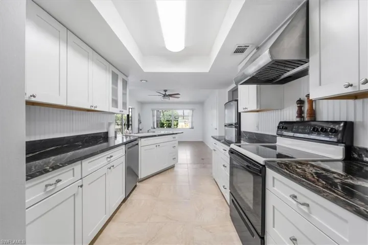 Kitchen with a raised ceiling, exhaust hood, dishwasher, a sink, and black electric range oven