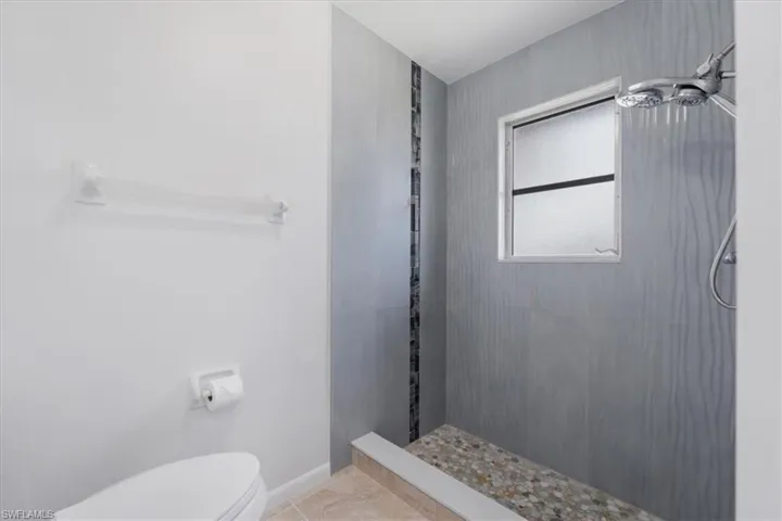 Full bathroom featuring toilet, tiled shower, and baseboards