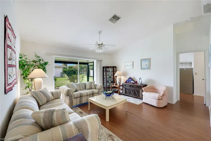 Living room with wood finished floors, lofted ceiling, ceiling fan, and visible vents