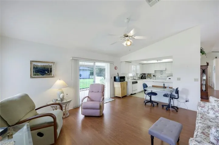 Living area with ceiling fan, visible vents, vaulted ceiling, and wood finished floors