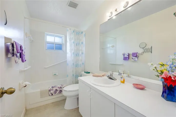 Bathroom featuring toilet, shower / bathtub combination with curtain, vanity, and visible vents