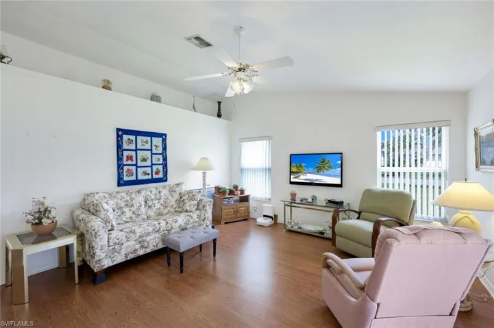 Living area with a ceiling fan, wood finished floors, vaulted ceiling, and visible vents