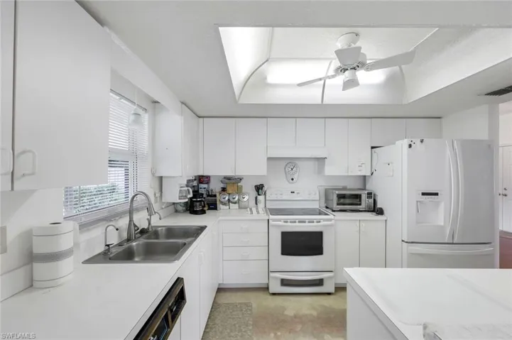Kitchen featuring white appliances, light countertops, a sink, and white cabinets