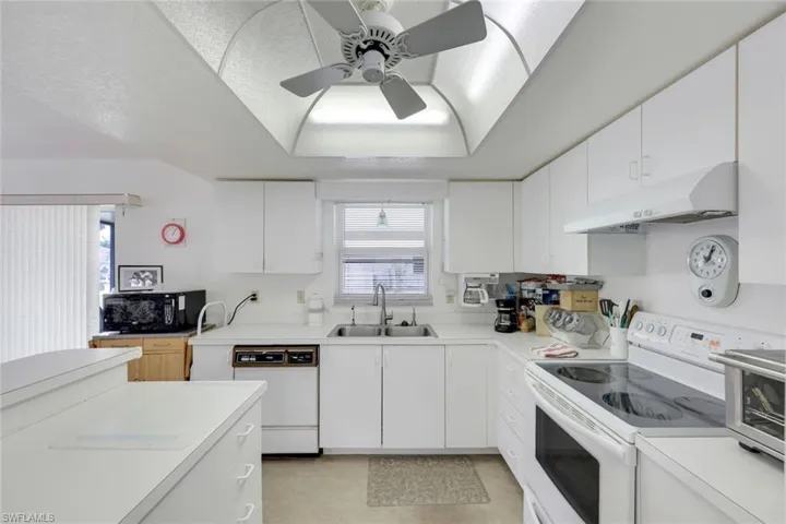 Kitchen featuring light countertops, a sink, under cabinet range hood, and white appliances
