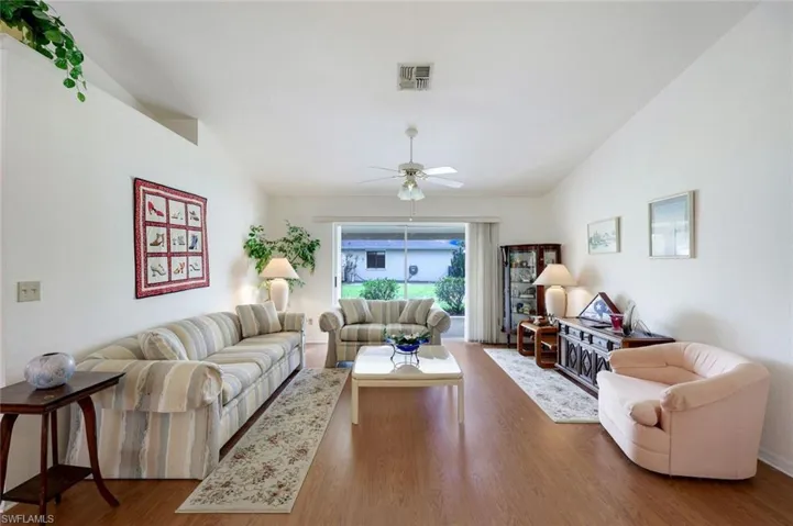 Living area with lofted ceiling, ceiling fan, visible vents, and wood finished floors