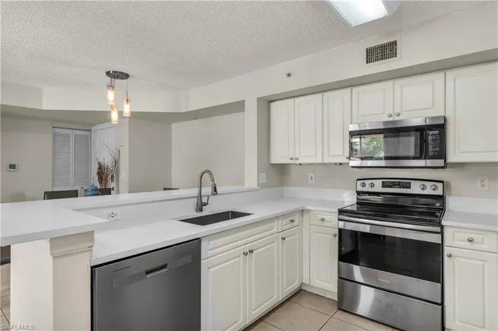 Kitchen featuring stainless steel appliances, a textured ceiling, white cabinets, hanging light fixtures, and a peninsula