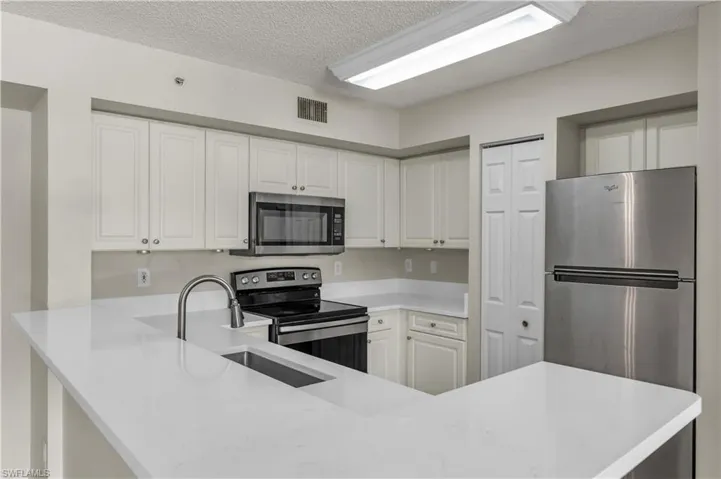 Kitchen featuring stainless steel appliances, a textured ceiling, white cabinetry, light stone countertops, and a peninsula