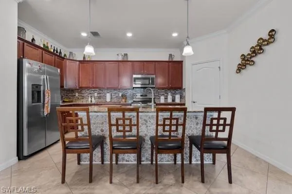 Kitchen featuring appliances with stainless steel finishes, a breakfast bar area, decorative backsplash, decorative light fixtures, and crown molding