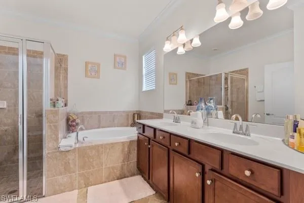 Bathroom with a stall shower, ornamental molding, double vanity, a garden tub, and light tile patterned floors