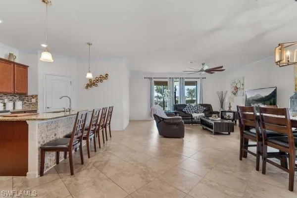 Dining area with crown molding, a chandelier, light tile patterned flooring, and a ceiling fan