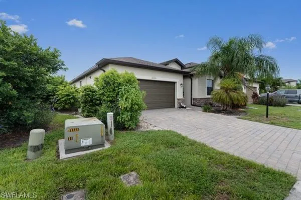 View of front of house with stucco siding, decorative driveway, an attached garage, a front yard, and stone siding