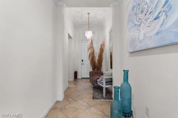 Corridor with a chandelier, crown molding, and light tile patterned floors