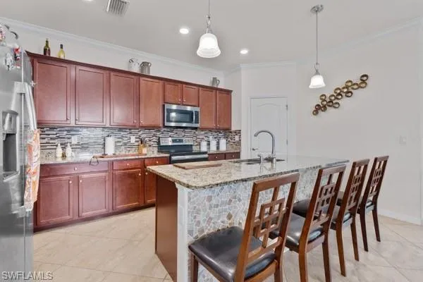 Kitchen featuring tasteful backsplash, light stone counters, appliances with stainless steel finishes, light tile patterned floors, and crown molding