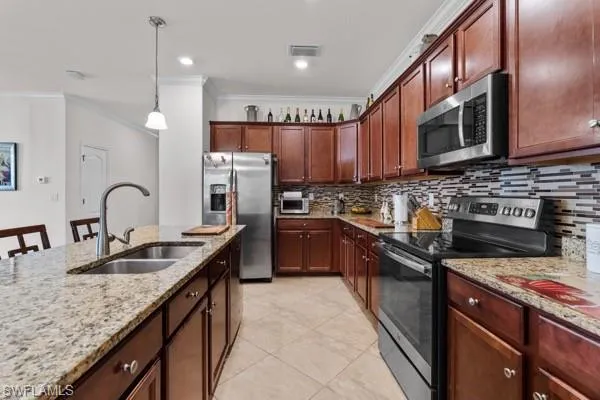 Kitchen with stainless steel appliances, crown molding, tasteful backsplash, hanging light fixtures, and light stone counters