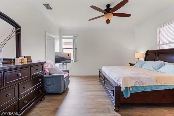 Bedroom with dark wood-style floors, crown molding, and ceiling fan