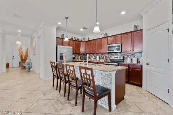 Kitchen featuring a breakfast bar area, appliances with stainless steel finishes, decorative light fixtures, a center island with sink, and backsplash