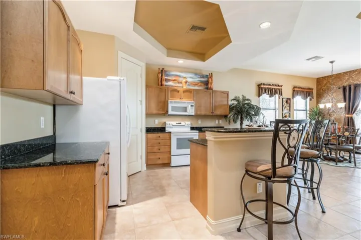 Kitchen featuring a breakfast bar, white appliances, a tray ceiling, dark stone countertops, and light tile patterned flooring