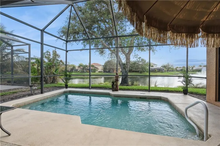 View of swimming pool featuring glass enclosure, a water view, and a patio