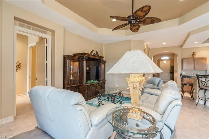 Living room with a tray ceiling, ceiling fan, and light tile patterned floors