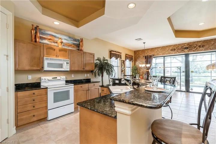 Kitchen featuring pendant lighting, white appliances, a center island with sink, sink, and a notable chandelier