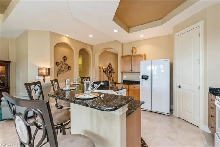 Kitchen with a tray ceiling, sink, a center island with sink, dark stone countertops, and white fridge with ice dispenser