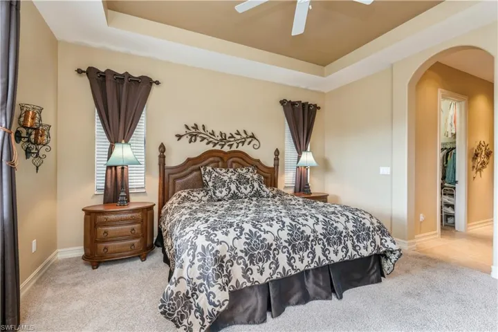 Bedroom featuring a raised ceiling, ceiling fan, a closet, and light colored carpet