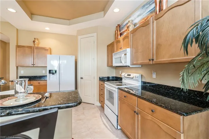 Kitchen with white appliances, a tray ceiling, and dark stone counters
