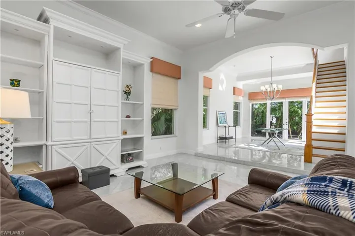 Living area with ornamental molding, a ceiling fan, arched walkways, and suspended lighting